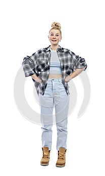 A funny young teenage girl stands with her hands on her belt. Laughing blonde girl in jeans, blue top and plaid shirt. Isolated on