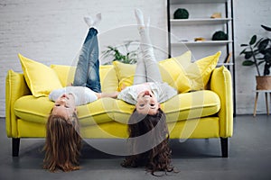 Funny young teenagers lying on yellow sofa and looking straigt on camera. They smile. Girls hold legs up in air. Their photo