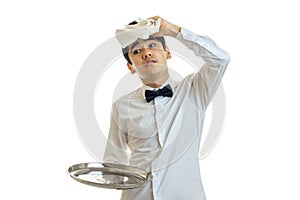 Funny young waiter`s shirt keeps empty tray and applies the napkin to head