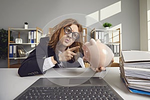 Funny young weird man accountant pointing at piggy bank with finger