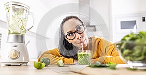 A funny young woman drinks a green smoothie that she made herself