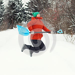 Funny young woman jump with snow shovel on rural road. Winter seasonal concept. Square
