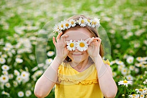 A funny young girl in a wreath of daisies laughs and holds flowers in front of her eyes. The screen is covered with flowers. In a