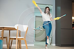 Funny young woman in yellow gloves dancing with the mop and singing while washing kitchen floor feeling happy