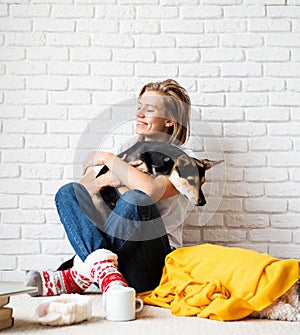 Funny young woman in yellow plaid sitting on the floor hugging her dog