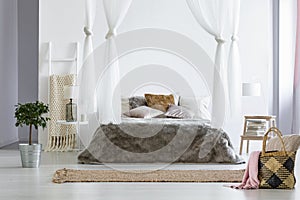 Fur coverlet placed on king-size bed with cushions and canopy in