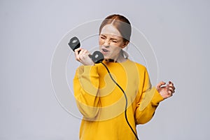 Furious angry young woman in stylish yellow sweater talking on retro phone and screaming in handset.