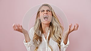 Furious blonde damsel, standing agitated over pink wall, lets out a crazy yell! her arms raised, the mad expression of frustration