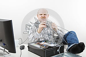 Furious Businessman Holding Tangled Cables Of Computer At Desk