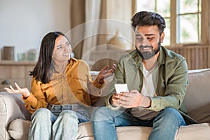 Furious indian wife scolding her dishonest husband using smartphone, woman looking for attention from boyfriend