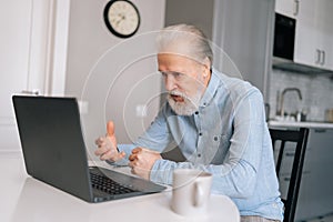 Furious irritated aged gray-haired businessman working from home office, angry face expression, gesturing. Angry senior