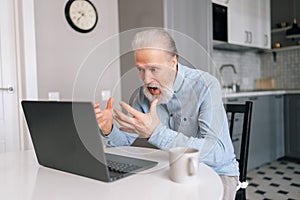 Furious irritated bearded mature elderly male working from home office, angry face expression, gesturing. Angry senior