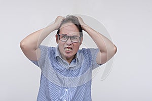 A furious and livid middle aged asian man pulling his hair in pure rage. Going amok after being stressed out. Isolated on a white