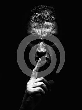 Furious mature man with an aggressive look making the silence sign in a violent and threatening way.