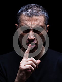 Furious mature man with an aggressive look making the silence sign in a violent and threatening way