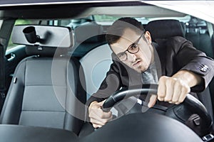 Furious young driver is looking through the windsheeld. He is driving his car and holding steering wheel with both hands