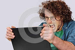 Furious young man with curly hair sitting at his desk with laptop feeling disappointed.