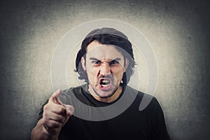 Furious young man pointing forefinger to camera blaming someone as guilty, or scolding  on grey wall background. Angry guy