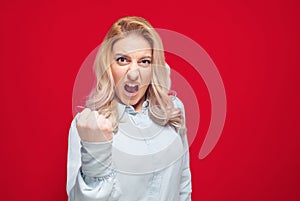 Furious young woman shows fist, isolated on red background. Rage girl