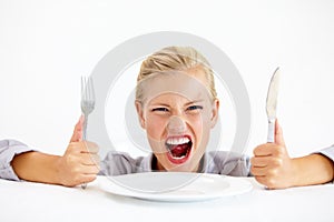 This is ridiculous Im starving. Furious young woman sitting in front of an empty plate while holding her knife and fork.
