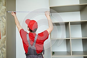 Furniture assembling. Professional worker measuring wardrobe aperture during installation at living room photo