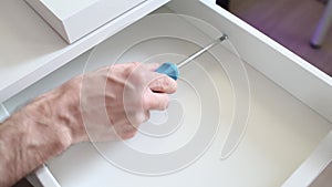 Furniture assembly process. Master assembles the bedside table. The worker uses a screwdriver. Close-up. Hand in frame.