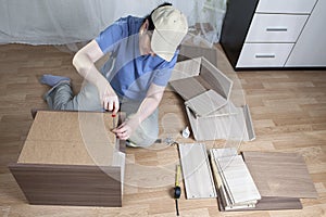 Furniture assembly, woman fastens sheet hardboard in back bedside table. photo