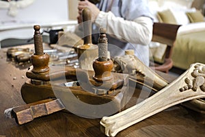 Furniture manufacturing with joiner tools, wooden decorative elements and carpenter, working with chisel at the background.