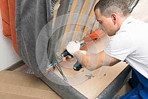 A furniture repair worker replacing the creaking mechanism of an upholstered sofa photo