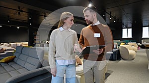 Furniture store manager with catalog demonstrates furniture to female buyer
