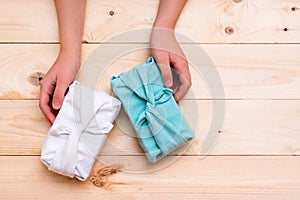 Furoshiki eco-friendly gifts wrapped in cloth and children`s hands on a wooden background. Zero waste. Top view