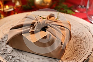 Furoshiki technique. Gift packed in beige fabric, blank card and festive decor on plate, closeup