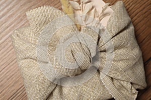 Furoshiki technique. Gift packed in beige fabric with dry leaves on wooden table, top view