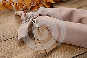 Furoshiki technique. Gift packed in beige fabric with tags on wooden table, closeup
