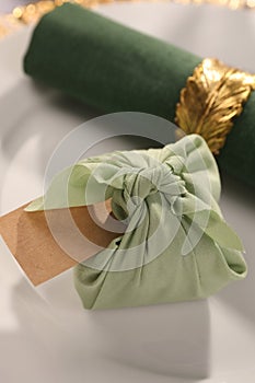 Furoshiki technique. Gift packed in green fabric, blank card and napkin on plate, closeup