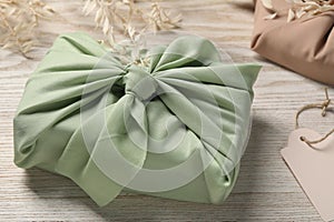 Furoshiki technique. Gift packed in green fabric and dried branches on white wooden table, closeup