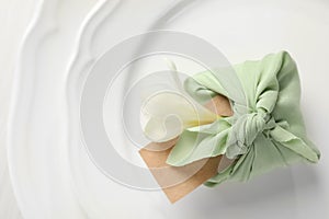 Furoshiki technique. Gift packed in green fabric with flower and blank card on plate, top view