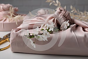 Furoshiki technique. Gift packed in pink fabric and beautiful flowers on white table, closeup