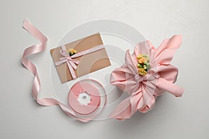 Furoshiki technique. Gift packed in pink fabric, card, flowers and ribbon on white table, flat lay