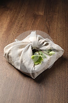 Furoshiki technique. Gift packed in white fabric decorated with beautiful flowers on wooden table