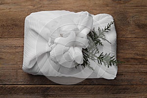 Furoshiki technique. Gift packed in white fabric and thuja branches on wooden table, top view