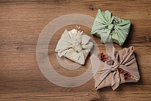 Furoshiki technique. Gifts packed in fabric and dry leaves on wooden table, flat lay. Space for text