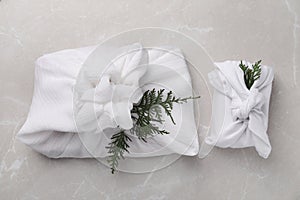 Furoshiki technique. Gifts packed in white fabric and thuja branches on grey marble table, flat lay