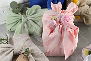 Furoshiki technique. Many gifts packed in fabric on grey table, closeup