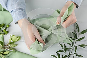 Furoshiki technique. Woman wrapping gift in green fabric at white table, top view