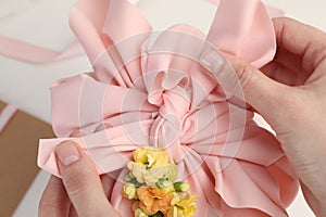 Furoshiki technique. Woman wrapping gift in pink fabric with flowers at white table, closeup