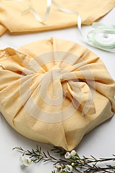 Furoshiki. Things packed in fabric, ribbon and flowers on white table, closeup