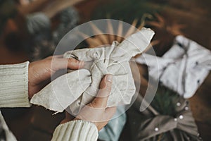 Furoshiki wrap, zero waste Christmas holidays. Hands holding christmas gift wrapped in modern festive fabric on rustic wooden