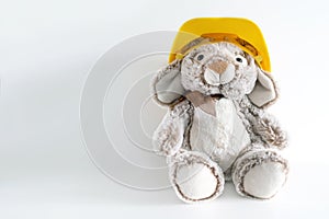 Furry, cuddly, cute little rabbit toy in yellow helmet on white background with copy space