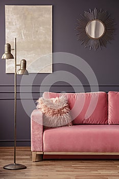 Furry pillow on a powder pink sofa, elegant golden sunburst mirror and marble painting on a dark gray wall in a living room inter